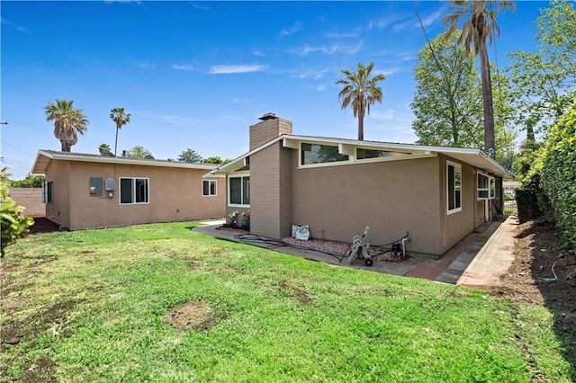 rear view of property with a lawn, stucco siding, and a chimney