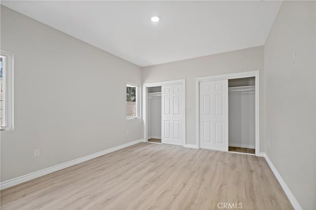 unfurnished bedroom featuring two closets, recessed lighting, baseboards, and light wood-style floors