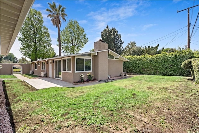 back of property with fence, a patio, stucco siding, a chimney, and a yard
