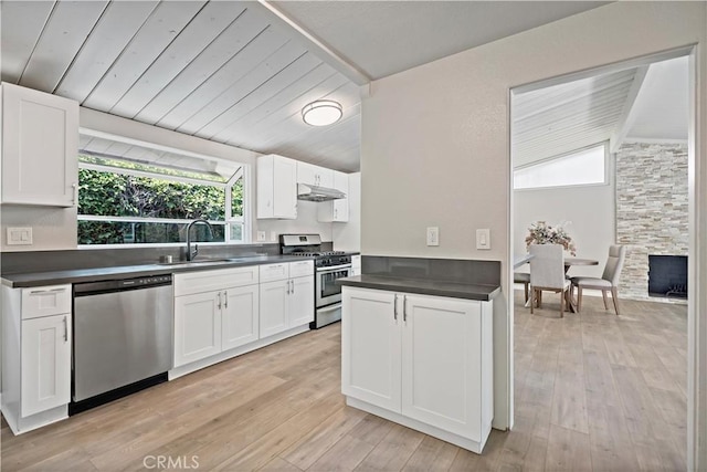 kitchen with dark countertops, a sink, stainless steel appliances, white cabinetry, and under cabinet range hood