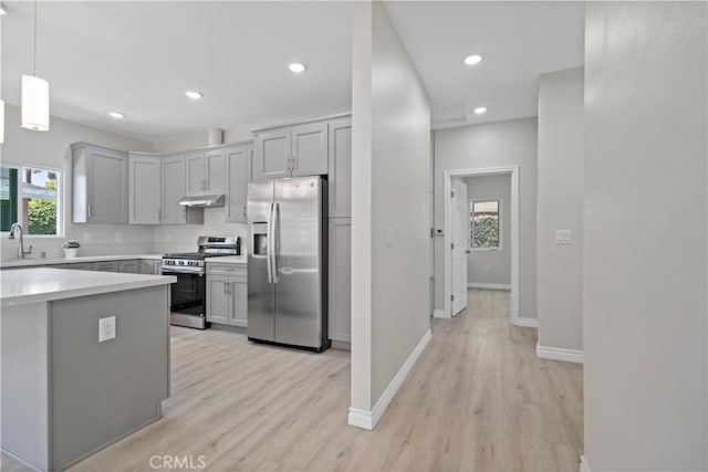 kitchen featuring appliances with stainless steel finishes, a sink, light wood finished floors, light countertops, and under cabinet range hood