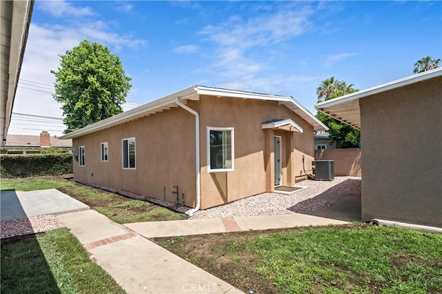 view of home's exterior with fence, stucco siding, central AC unit, a patio area, and a yard