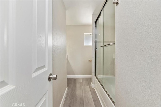 full bath with baseboards, a textured wall, combined bath / shower with glass door, and wood finished floors