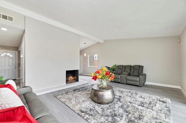 living room featuring visible vents, baseboards, vaulted ceiling with beams, wood finished floors, and a lit fireplace