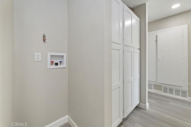 clothes washing area featuring washer hookup, visible vents, cabinet space, baseboards, and light wood-style floors