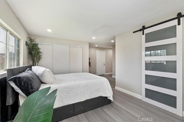 bedroom with a barn door, wood finished floors, baseboards, a closet, and recessed lighting