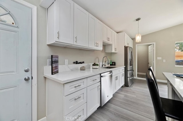 kitchen with a sink, light countertops, stainless steel appliances, baseboards, and white cabinetry