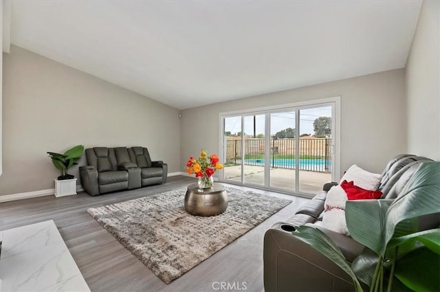living area with baseboards, wood finished floors, and vaulted ceiling