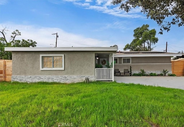 rear view of house with fence, stucco siding, a yard, and solar panels