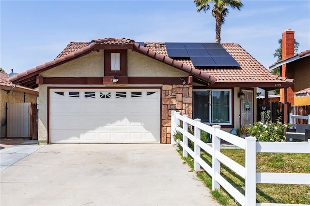 view of front of property featuring a tiled roof, fence, roof mounted solar panels, concrete driveway, and an attached garage