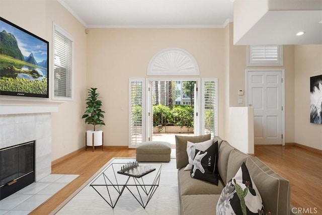living room with crown molding, baseboards, a tiled fireplace, and wood finished floors
