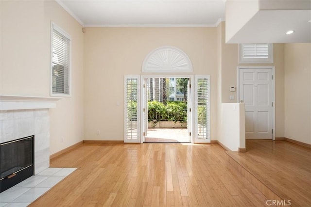 unfurnished living room featuring baseboards, ornamental molding, light wood finished floors, and a tile fireplace