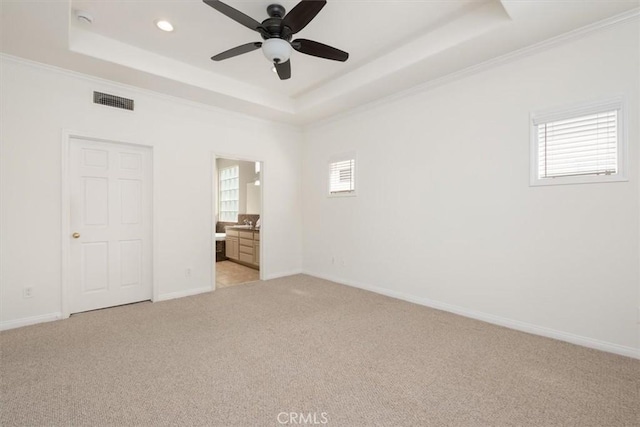 unfurnished bedroom featuring light colored carpet, a tray ceiling, visible vents, and multiple windows