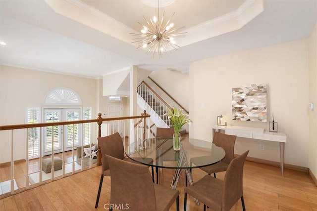 dining area with baseboards, a notable chandelier, light wood-style flooring, and a raised ceiling