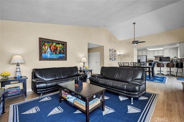 living area featuring a ceiling fan, light wood finished floors, and vaulted ceiling