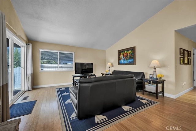 living area featuring baseboards, vaulted ceiling, light wood-style flooring, and visible vents