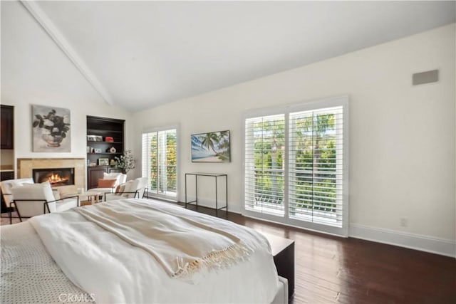 bedroom with lofted ceiling with beams, a glass covered fireplace, access to exterior, baseboards, and wood finished floors