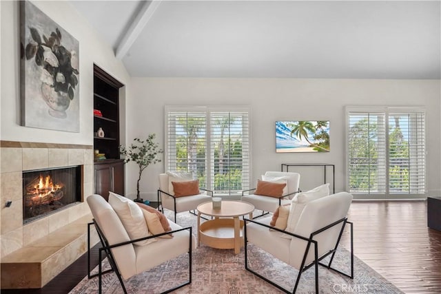 living area featuring a tiled fireplace, vaulted ceiling with beams, plenty of natural light, and wood finished floors