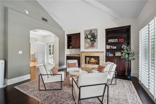 living area featuring visible vents, arched walkways, dark wood finished floors, a tile fireplace, and baseboards