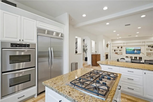 kitchen with stainless steel appliances, arched walkways, visible vents, and light stone counters