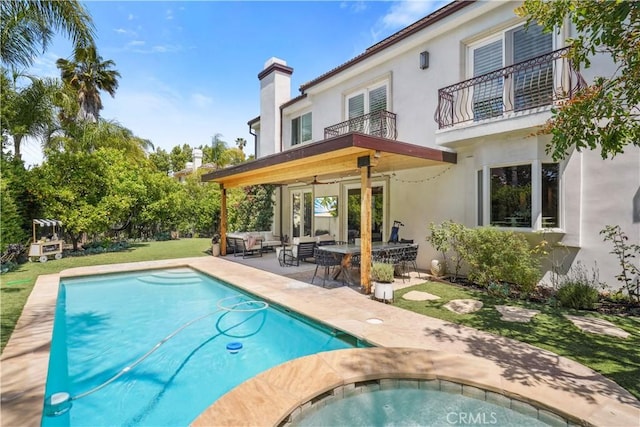 rear view of house with a patio, an outdoor pool, stucco siding, and a balcony