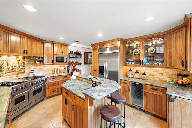 kitchen featuring light stone countertops, stone tile floors, beverage cooler, backsplash, and appliances with stainless steel finishes
