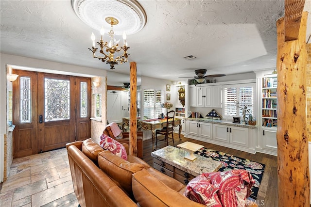 living room with a wealth of natural light, visible vents, ceiling fan with notable chandelier, and a textured ceiling