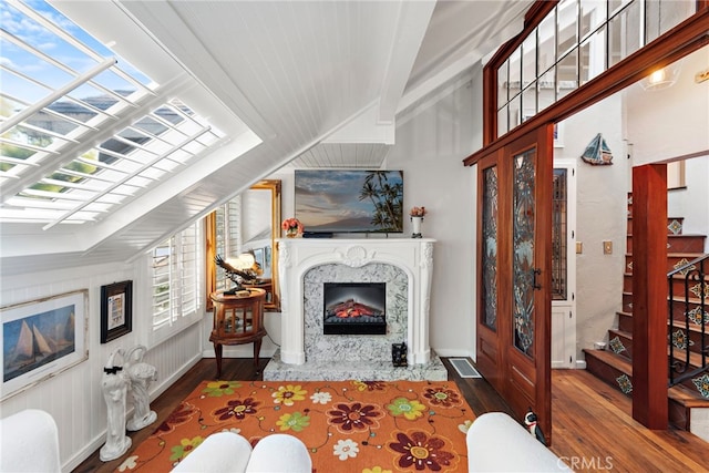 living room featuring wood finished floors, a fireplace, stairway, lofted ceiling with skylight, and baseboards