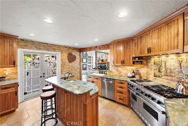 kitchen with a sink, stainless steel appliances, tasteful backsplash, stone tile flooring, and a breakfast bar area