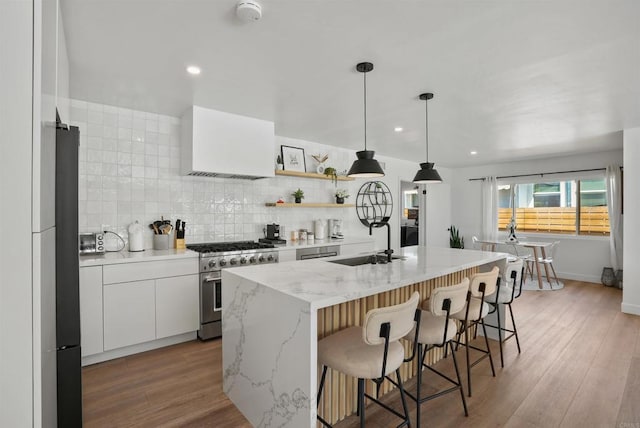 kitchen with decorative backsplash, a kitchen breakfast bar, a sink, stainless steel range, and white cabinets