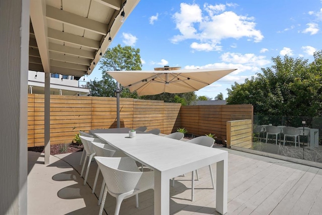 view of patio with fence, a wooden deck, and outdoor dining space