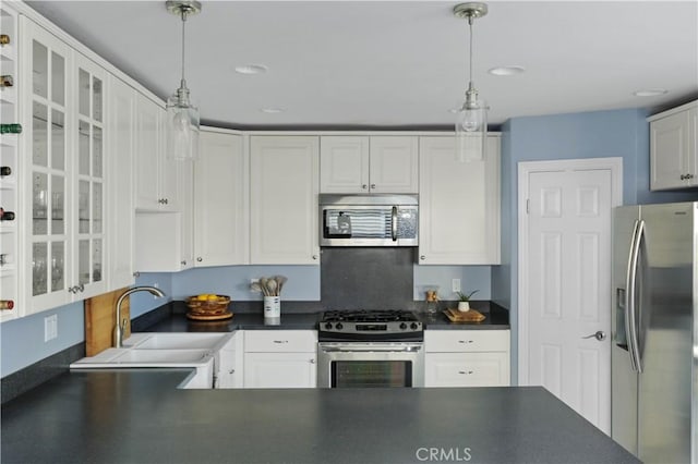 kitchen with dark countertops, a sink, white cabinets, glass insert cabinets, and stainless steel appliances