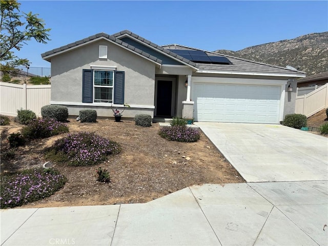 ranch-style house featuring concrete driveway, fence, solar panels, and a garage