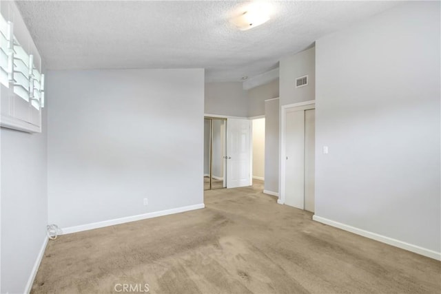 carpeted empty room with a textured ceiling, vaulted ceiling, baseboards, and visible vents