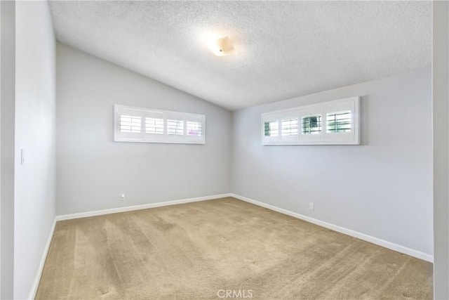 empty room with carpet floors, a textured ceiling, baseboards, and lofted ceiling