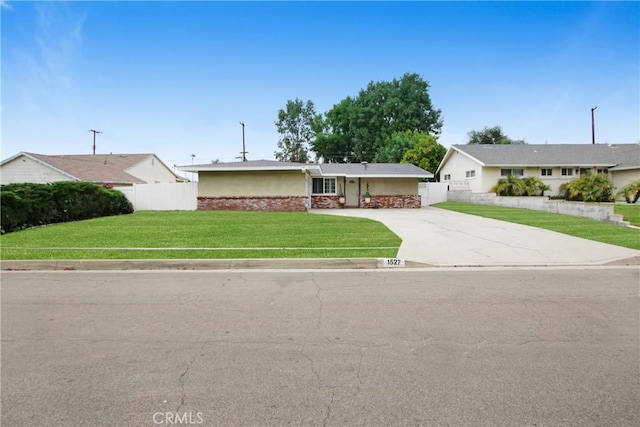 ranch-style home featuring concrete driveway, fence, stone siding, and a front lawn