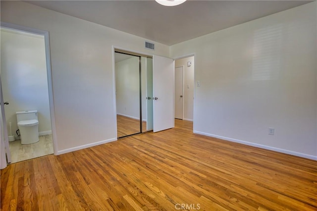 unfurnished bedroom featuring baseboards, visible vents, wood finished floors, and ensuite bath