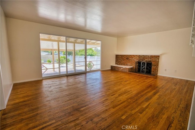 unfurnished living room with baseboards, a brick fireplace, and wood finished floors