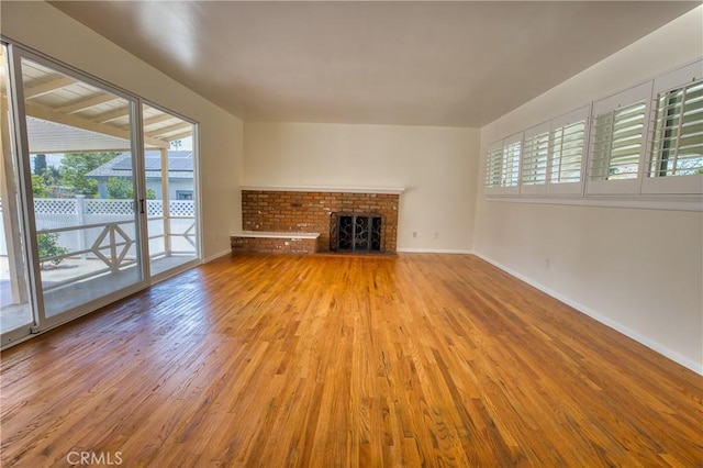 unfurnished living room featuring baseboards, a brick fireplace, and wood finished floors