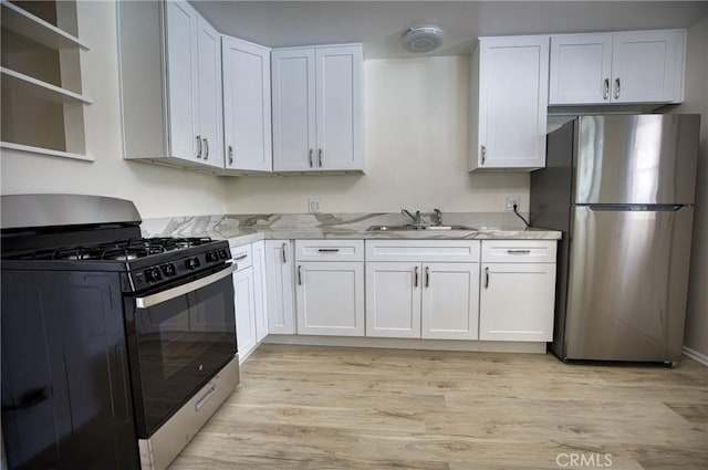 kitchen featuring freestanding refrigerator, white cabinets, a sink, light wood finished floors, and gas stove