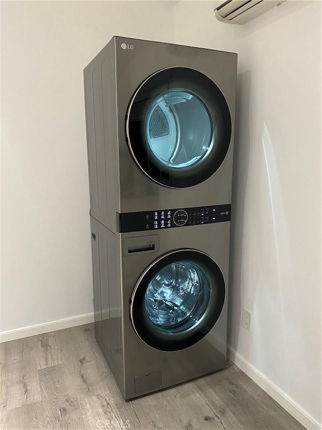 laundry room featuring laundry area, baseboards, stacked washer / dryer, wood finished floors, and a wall mounted AC