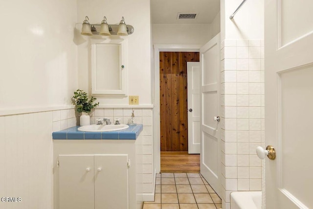 full bathroom with wooden walls, tile patterned floors, visible vents, and vanity