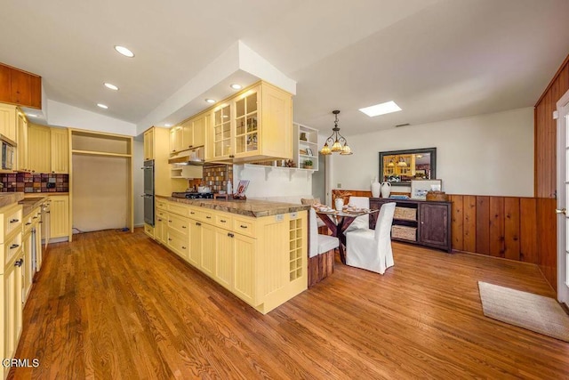 kitchen featuring backsplash, an inviting chandelier, glass insert cabinets, and wood finished floors