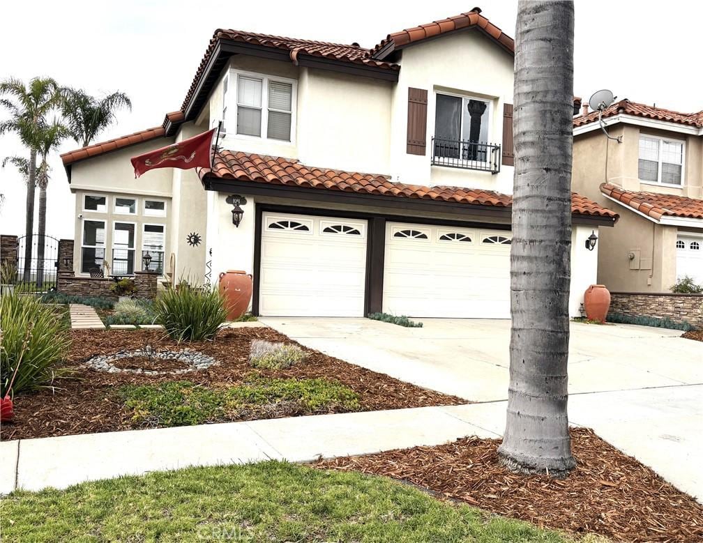 mediterranean / spanish home with a tile roof, a garage, stucco siding, concrete driveway, and a balcony