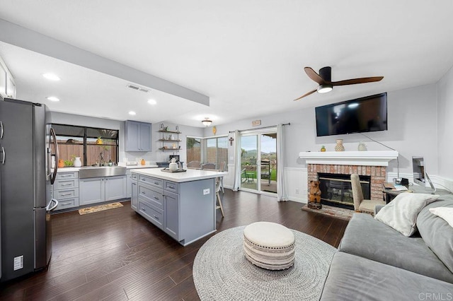 living room with a ceiling fan, dark wood-style floors, a brick fireplace, and visible vents