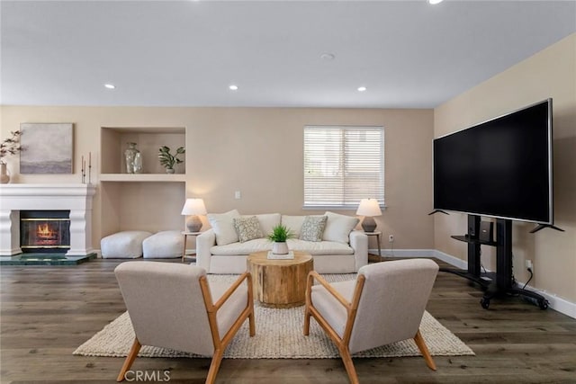 living area with a glass covered fireplace, baseboards, recessed lighting, and wood finished floors