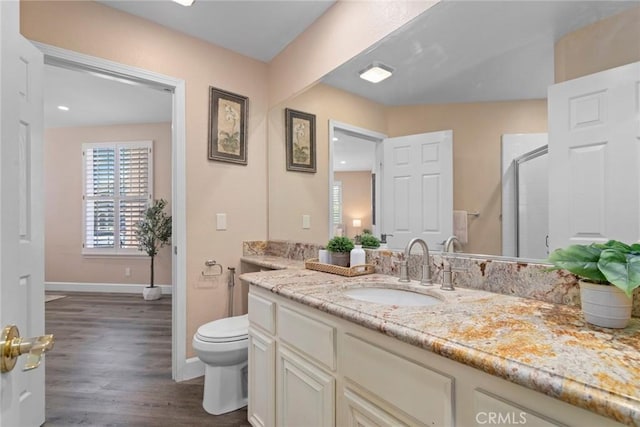 bathroom with vanity, a shower with door, wood finished floors, toilet, and baseboards