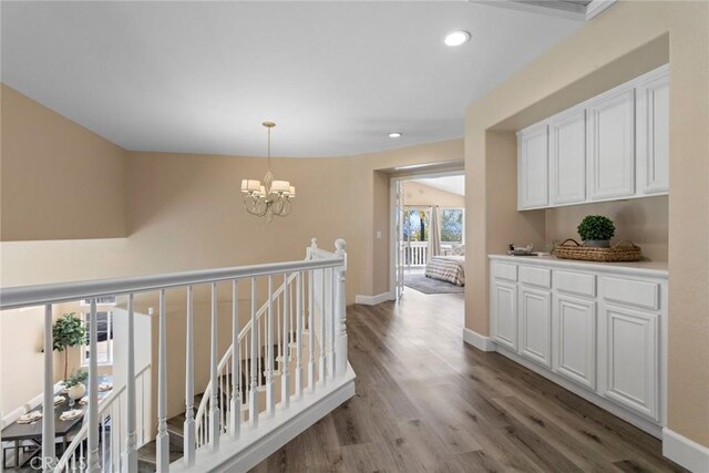 corridor with an inviting chandelier, wood finished floors, baseboards, recessed lighting, and an upstairs landing