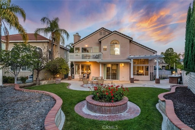 back of house at dusk featuring a patio, stucco siding, a yard, and a balcony