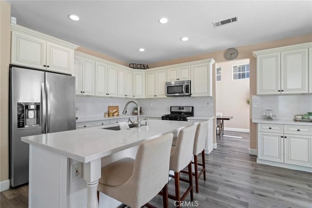 kitchen with visible vents, baseboards, a kitchen bar, a sink, and appliances with stainless steel finishes